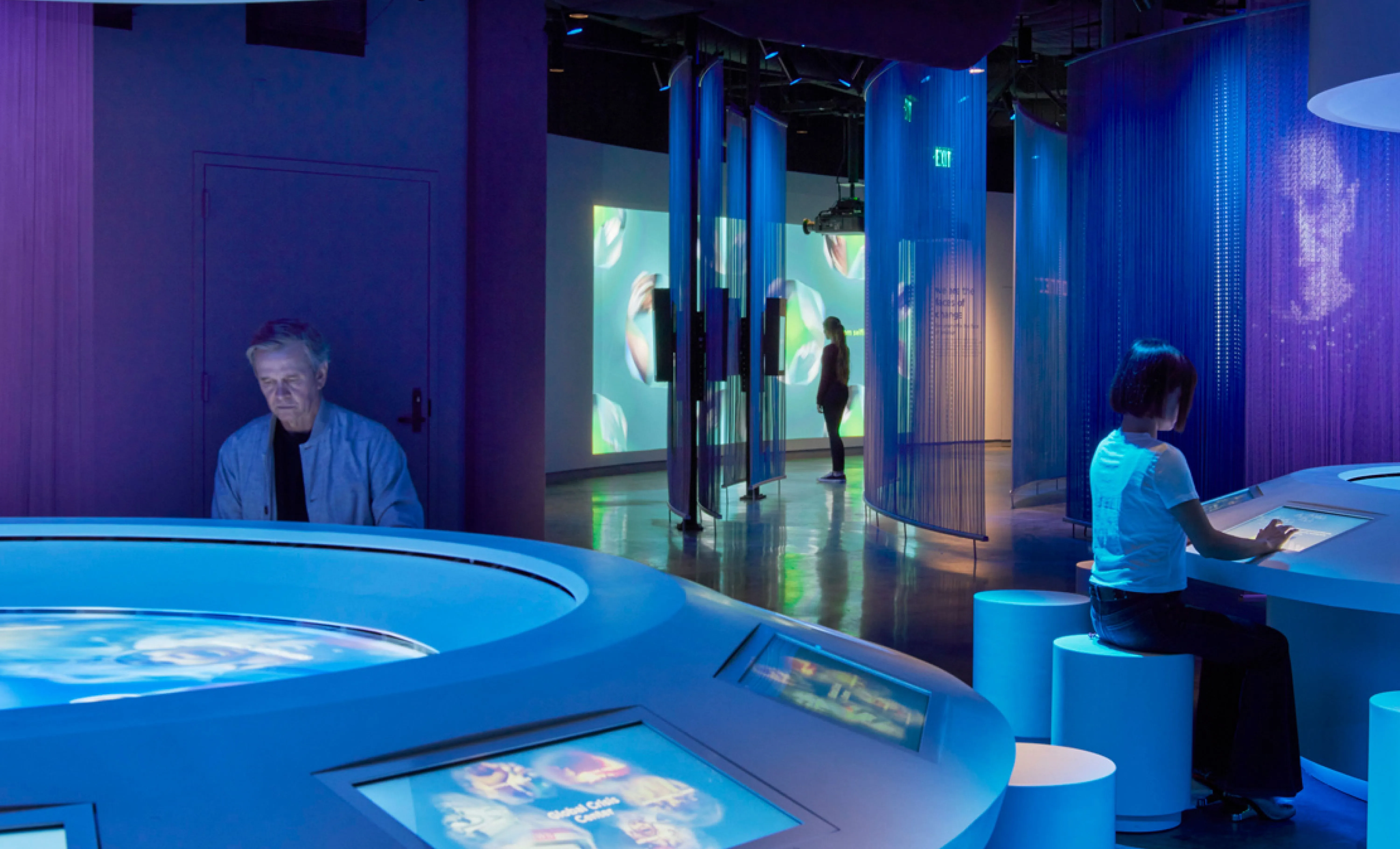 Visitors interacting with activity tables and watching films projected on the museum wall.
